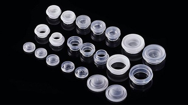 Small clear plastic container lids, various sizes for pharmaceuticals or cosmetics, arranged on black background.