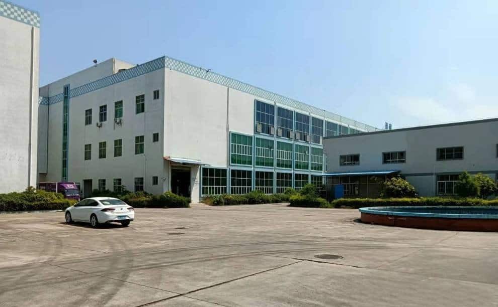 Modern office building with glass windows and parking lot in an industrial area during daytime.