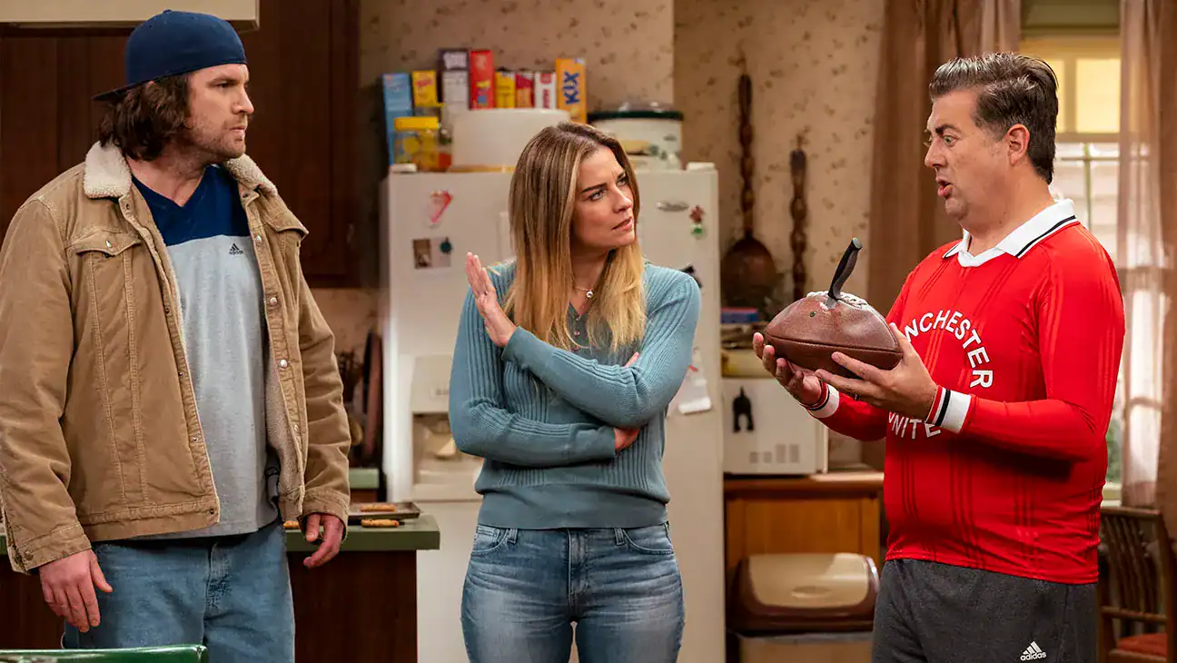 Cine de comedia familiar con personajes conversando en la cocina sobre una apuesta de fútbol, estilo sitcom, en un hogar acogedor.