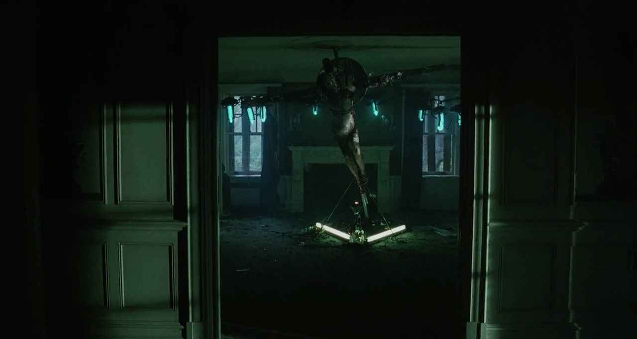 Hombre colgado en una habitación oscura con iluminación de neón, escena inquietante y misteriosa.