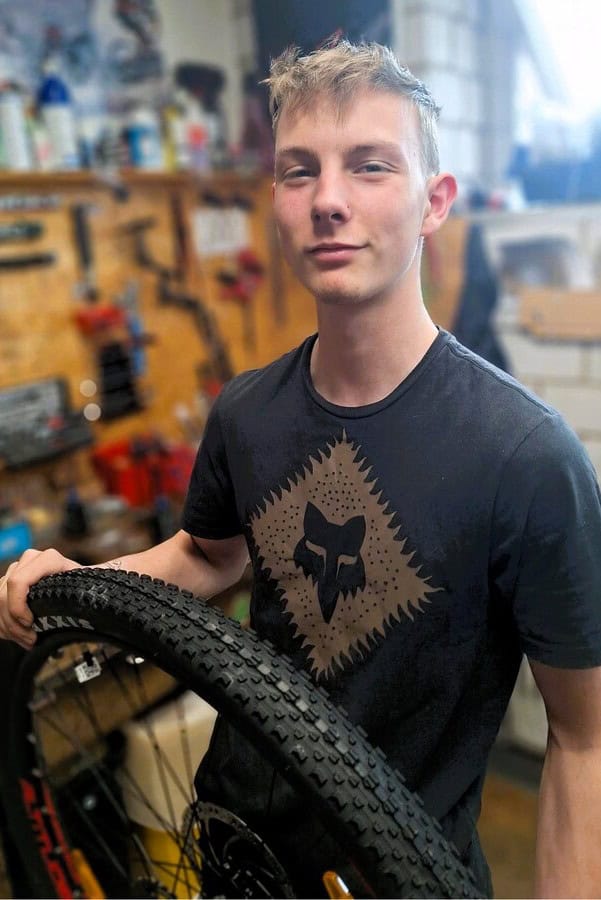 Junger Mitarbeiter bei Radfalk Radsport mit Fahrrad im Werkstattbereich.