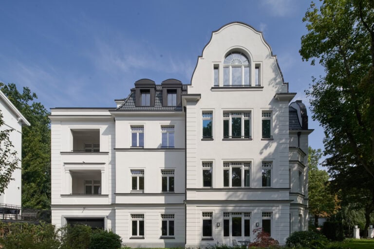 Elegantes Gebäude mit weißer Fassade, großen Fenstern und grünem Umfeld