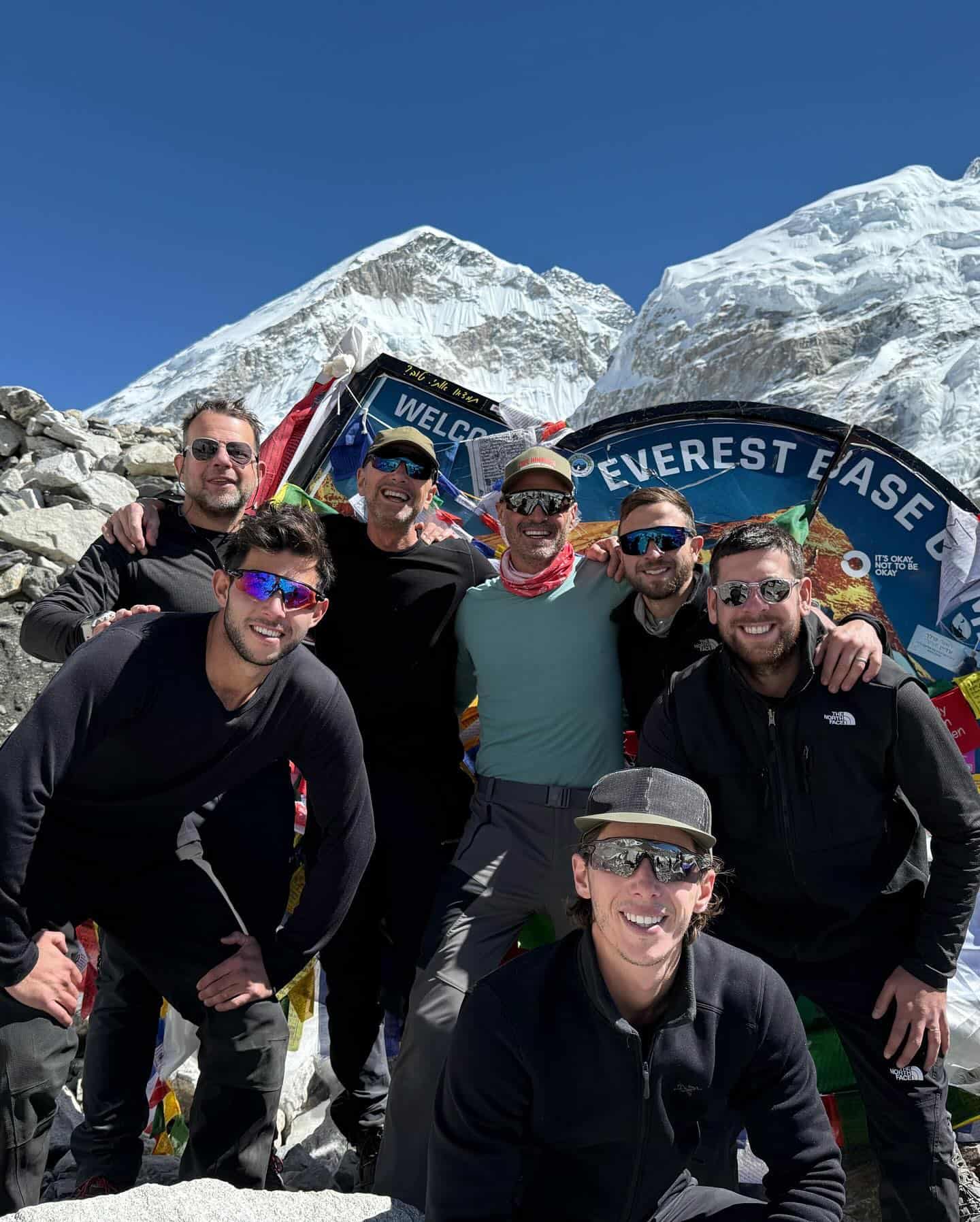 Men standing in front of an Everest Basecamp sign with mountains in the background