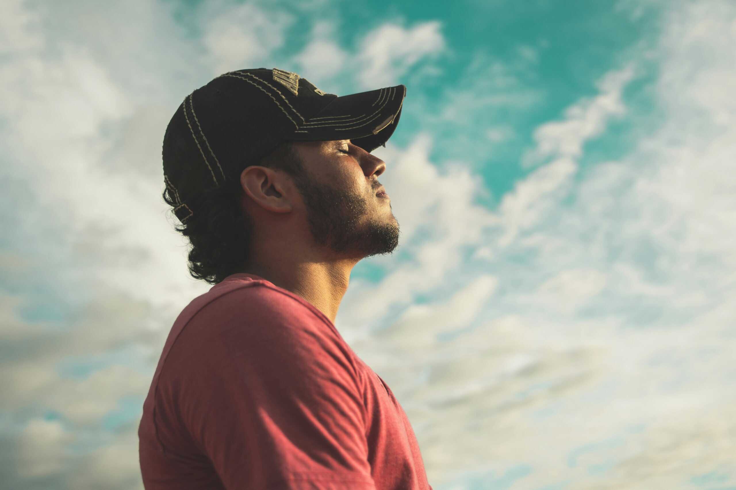 Man with cap doing breathwork meditation with the sky as the backdrop.