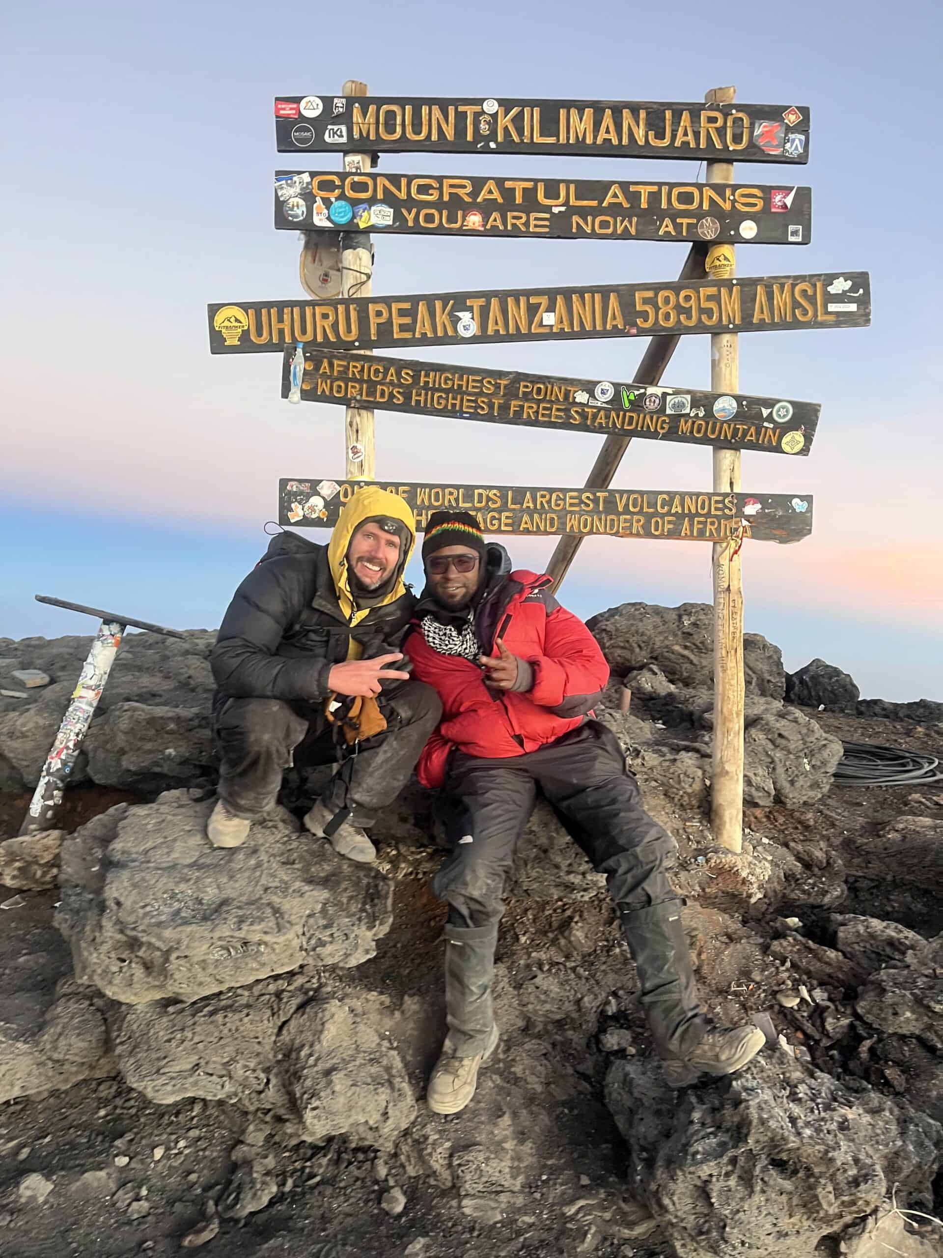 Anthony founder of Recal with a guide in front of the Kilimanjaro sign at the summit.