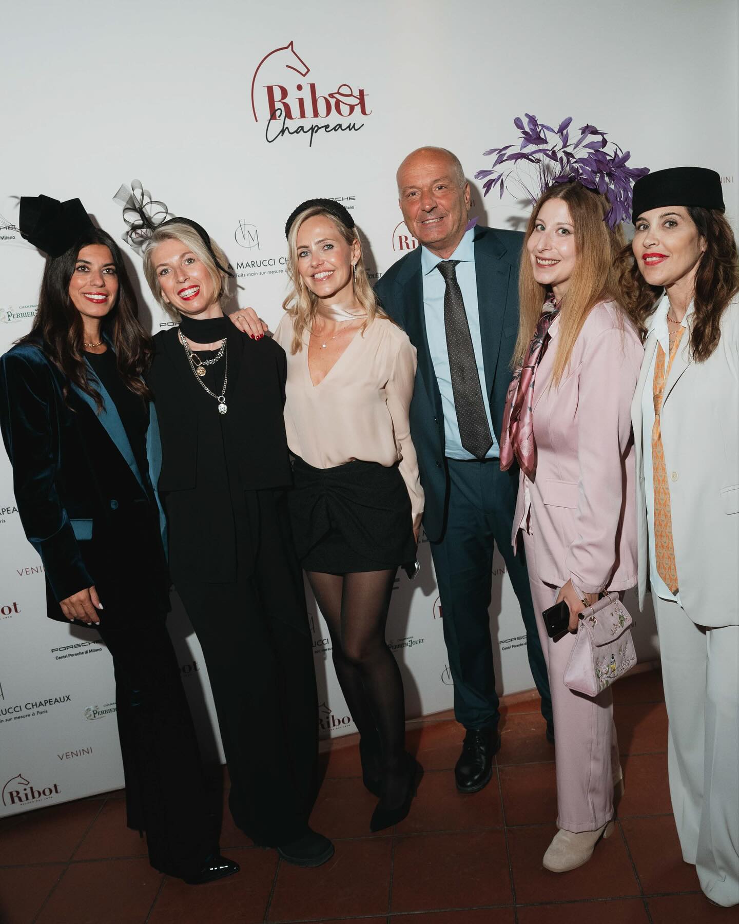 Gruppo di sei persone, uomini e donne, posano sorridenti davanti al backdrop Ribot Chapeau durante l’evento.