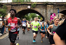 Runners participating in the Hackney Half Marathon, supporting the Single Homeless Project charity, with spectators and a historic bridge in the background.