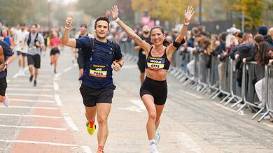 Two runners celebrating crossing the finish line at the Manchester Half Marathon, with cheering spectators and autumn trees in the background.