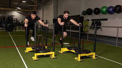 Two men performing sled push exercises in a gym, focusing on strength and endurance training for runners.