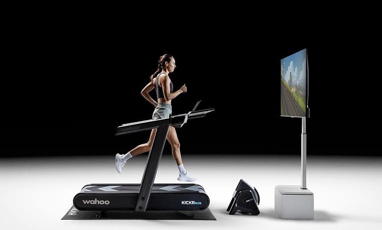 Woman running on a treadmill with virtual outdoor scenery on screen, showcasing indoor running and virtual training technology.