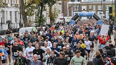 Large group of runners participating in the Stockport 10K race, with an archway and cityscape in the background.