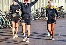 Group of runners celebrating with arms raised after completing a race in an urban setting with bicycles in the background.