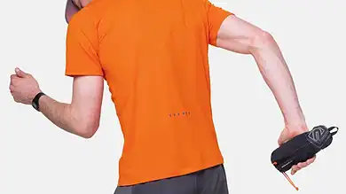 Close-up of a runner holding a Ronhill SoftFlask with Sleeve, wearing an orange shirt and grey shorts, preparing for a run.