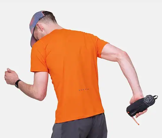Close-up of a runner holding a Ronhill SoftFlask with Sleeve, wearing an orange shirt and grey shorts, preparing for a run.