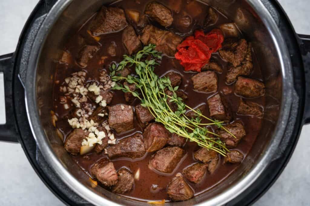 Instant pot with beef broth, seared beef chunks, garlic, tomato paste and fresh thyme.