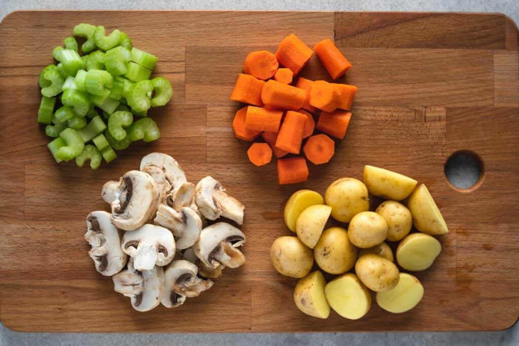 cutting board with chopped up celery, carrots, mushrooms, potatoes.
