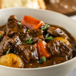 Bowl of beef stew with chunks of beef, carrots, and potatoes. Garnished with fresh thyme leaves