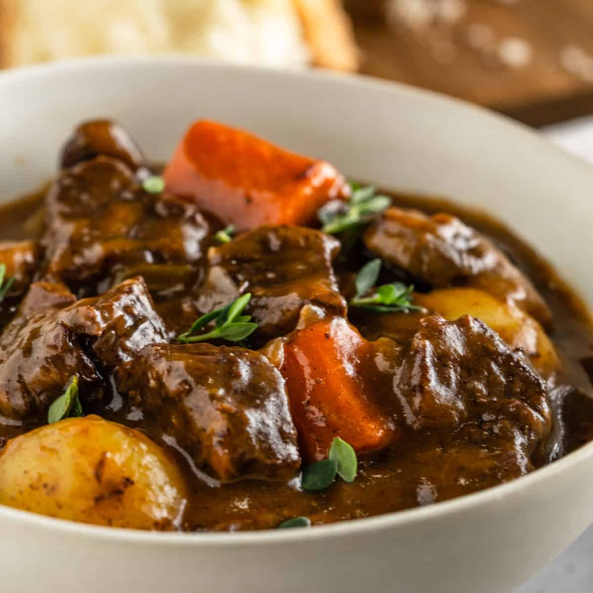 A bowl of beef stew with beef, carrots, potatoes and garnished with thyme