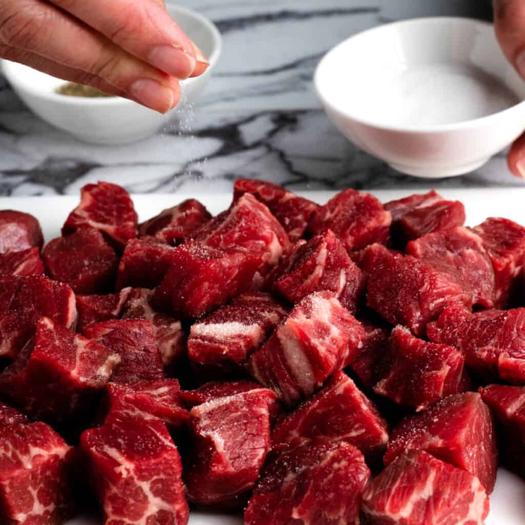 Hands sprinkling salt onto beef chunks