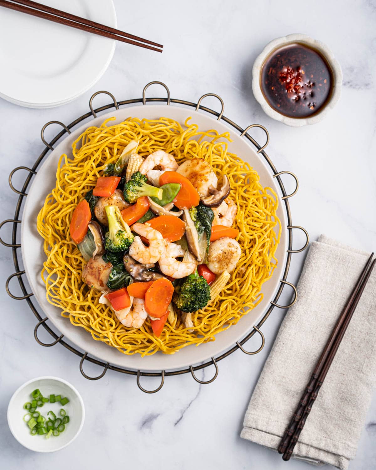 Plate of mi xao gion with stir fried shrimp, scallops, carrots, broccoli, baby corn, baby bok choy, mushrooms, red bell peppers, and onions.