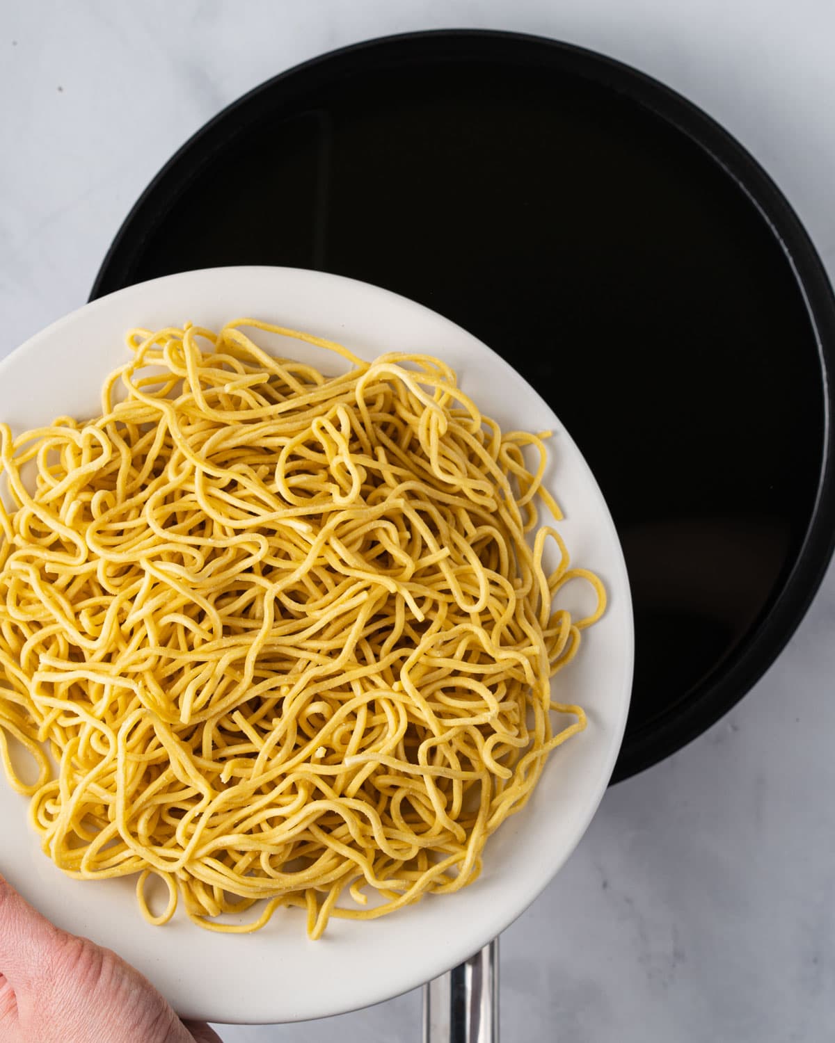 Adding fresh chow mein noodles into a pan of hot oil.