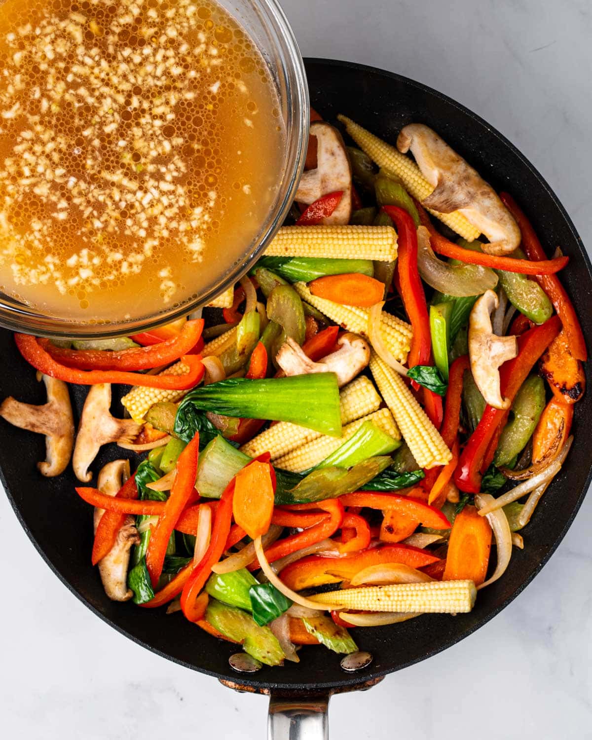 Pouring sauce on vegetables in a pan to make stir fry.