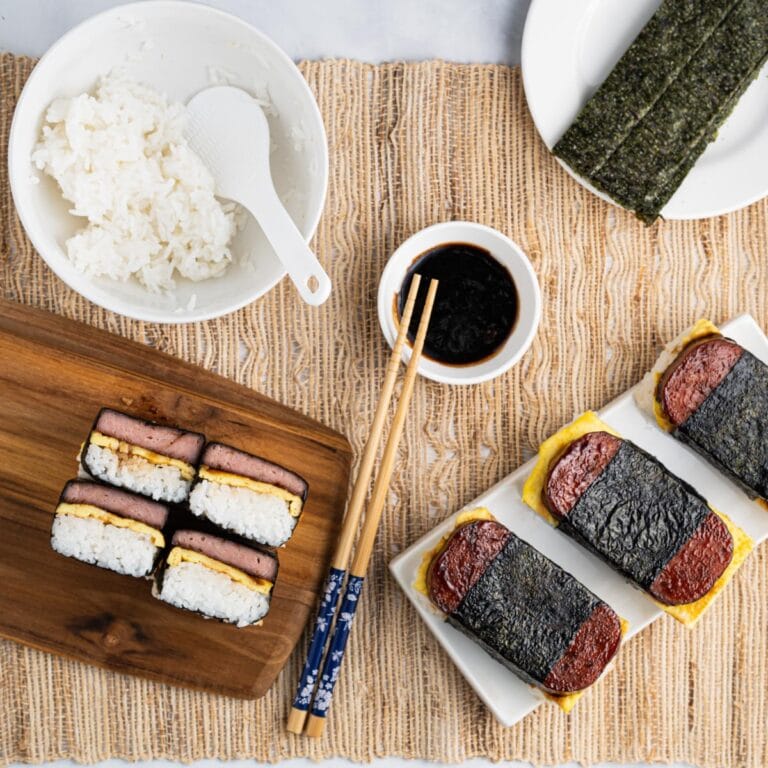 Spam musubi with eggs - crosssection on a cutting board and whole one on a plate.