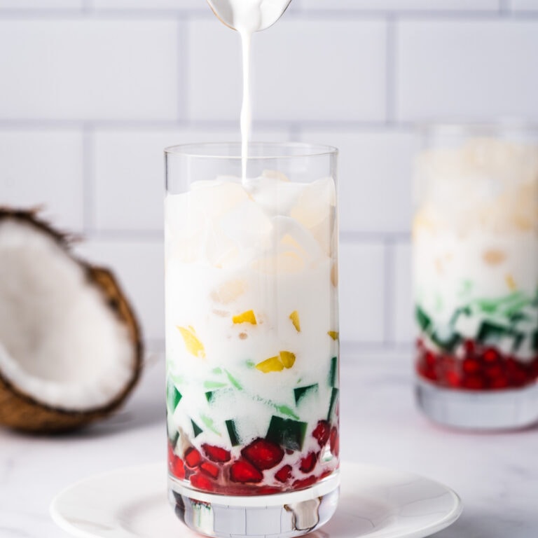 Two cups of Che Thai with a creamer pitcher pouring coconut milk sauce in.