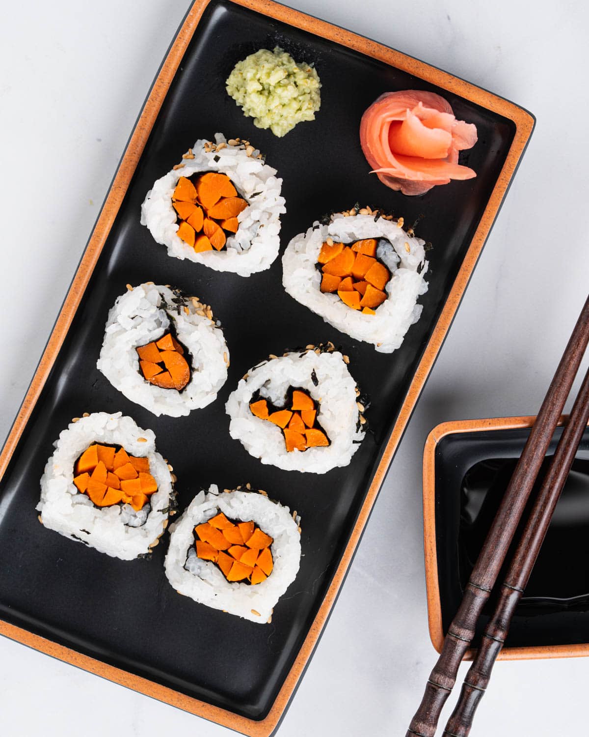 Plate of gobo sushi rolls with sides of wasabi, pickled ginger and soy sauce.