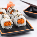 gobo sushi rolls on a plate with soy sauce and chopsticks on the side.