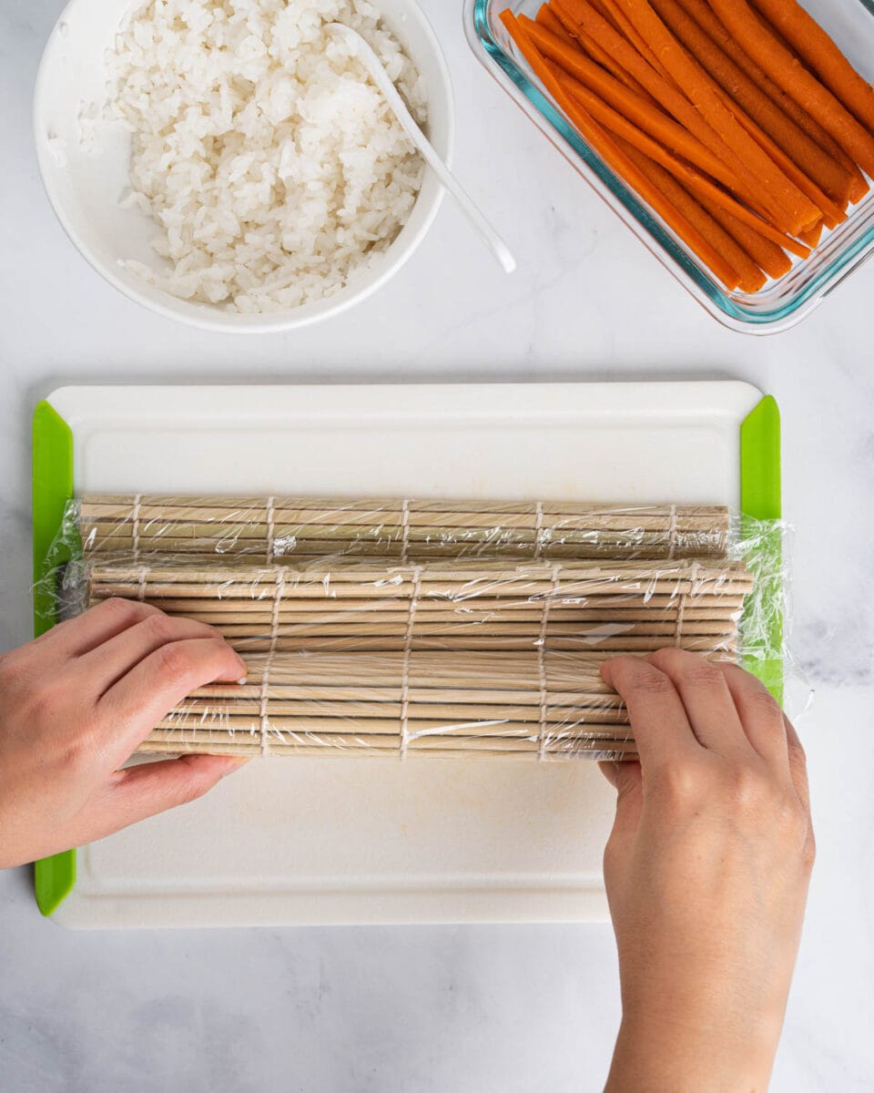 Hands rolling the gobo sushi roll with a sushi mat.