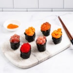 6 gunkan on a marble serving board: 1 tobiko gunkan, 2 tuna gunkans, 2 salmon gunkans and 1 ikura gunkan.