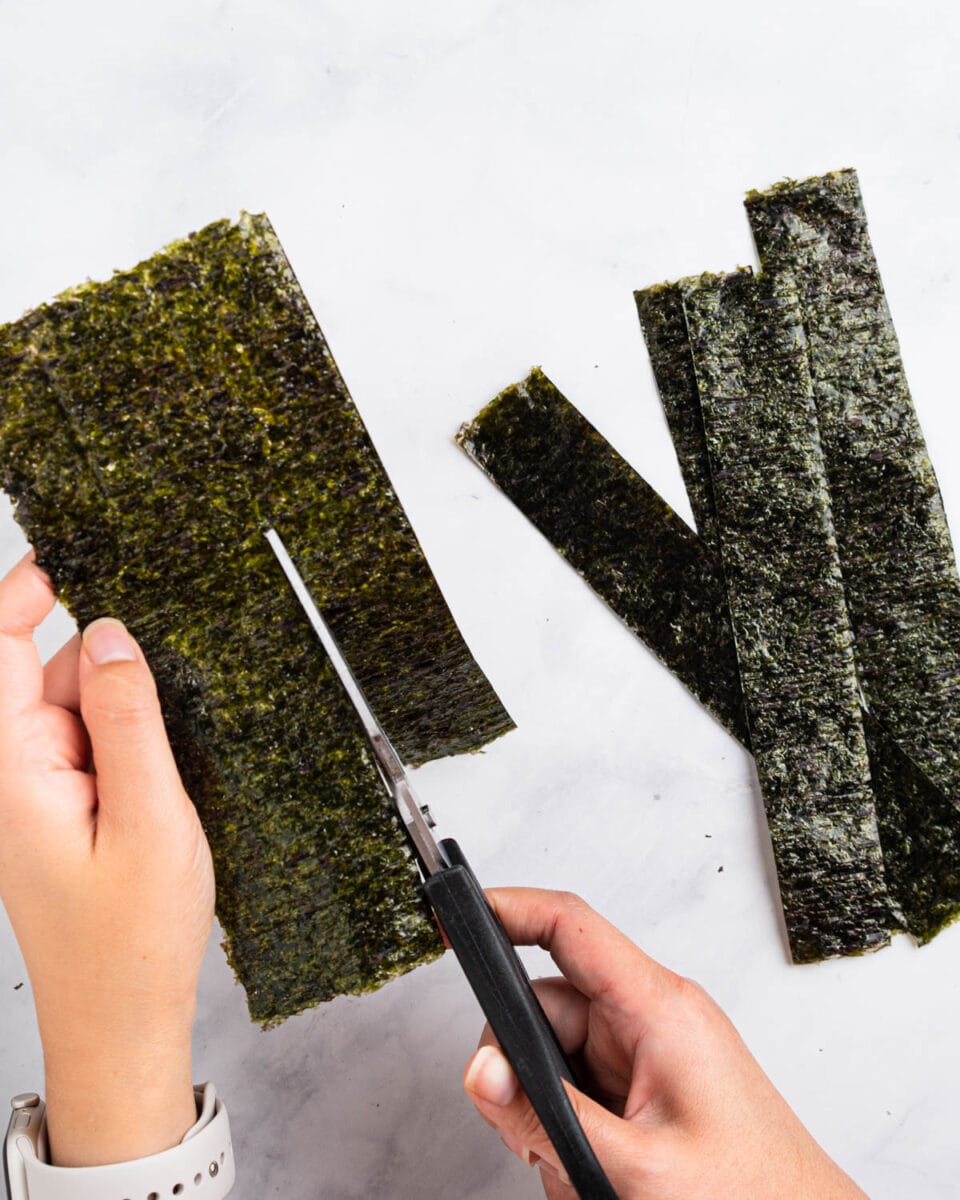 Scissors cutting the nori sheet into strips.