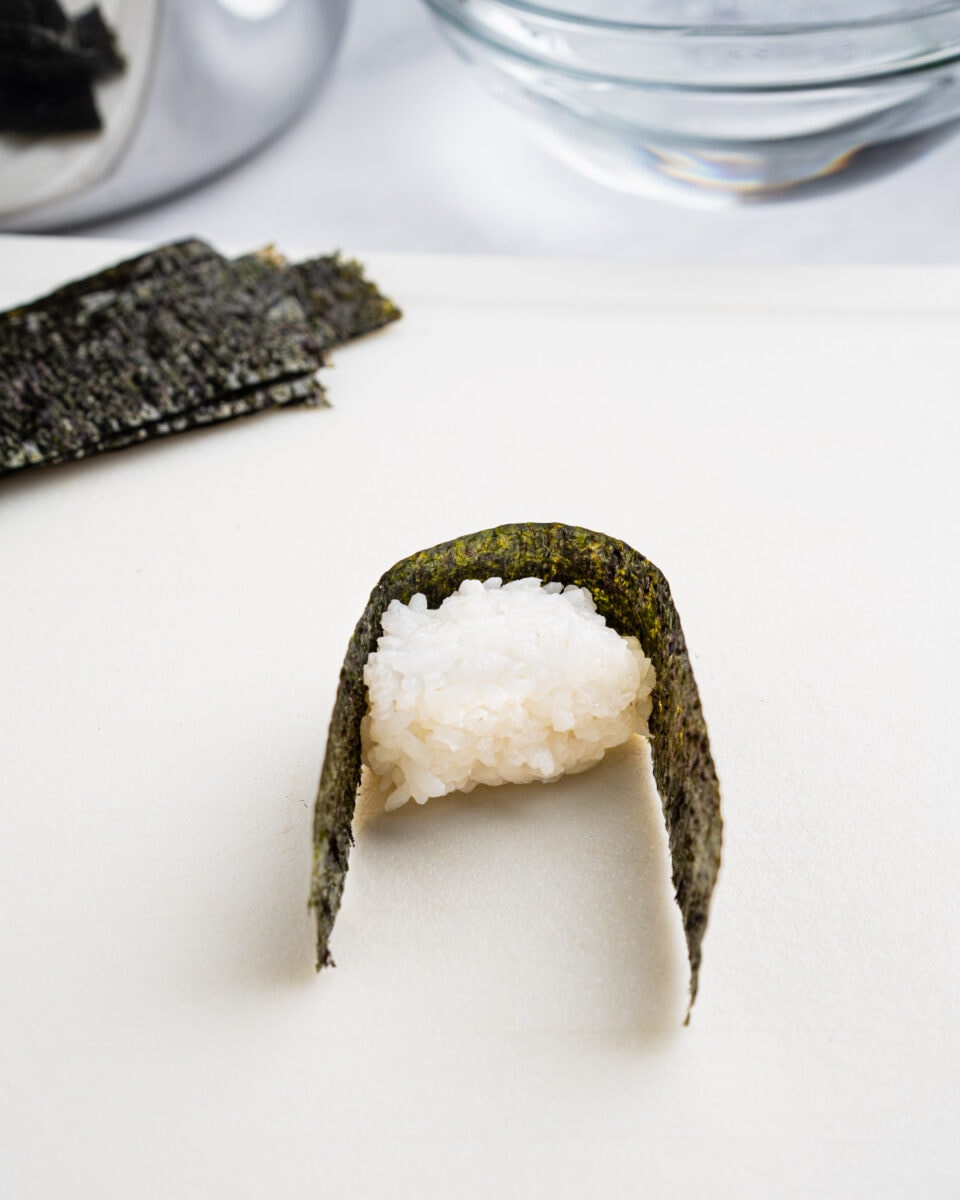 Wrapping the mound of rice with a strip of nori.