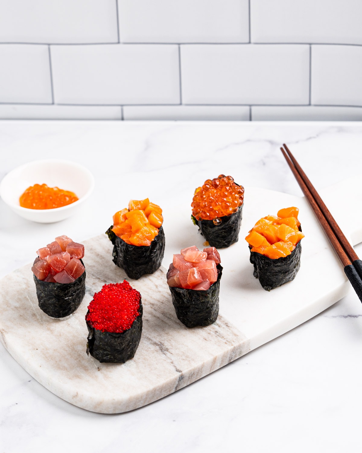 6 gunkan on a marble serving board: 1 tabiko gunkan, 2 tuna gunkans, 2 salmon gunkans and 1 ikura gunkan.