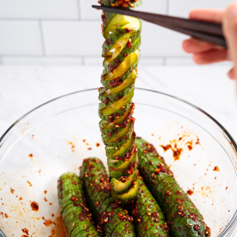 Spicy cucumber salad in a bowl and chopsticks holding up one spiral cucumber.