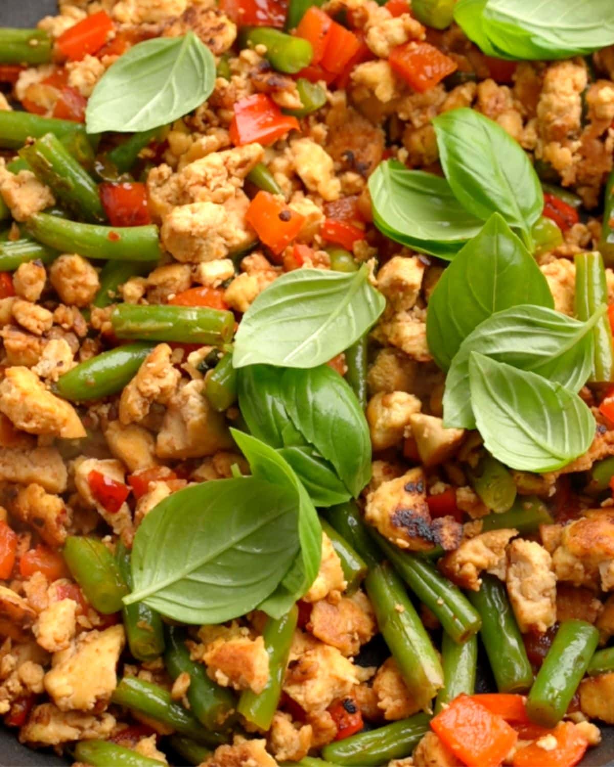 Stir fried pad kra pao with tofu in a pan with fresh basil on top.