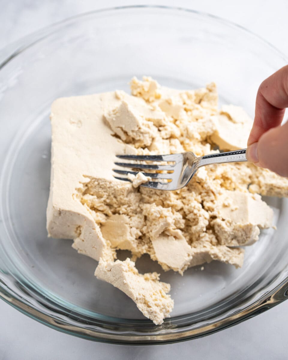 fork breaking up the tofu into smaller chunks.