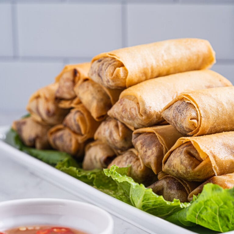 stacks on cha gio on a serving plate with a side dipping bowl of nuoc cham.