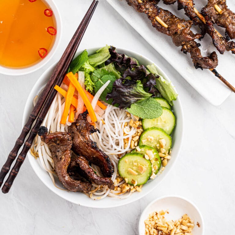 bowl of bun thit nuong with vermicelli noodles, fresh and pickled veggies, grilled pork and crushed peanuts. Side of nuoc cham and skewered grilled pork.