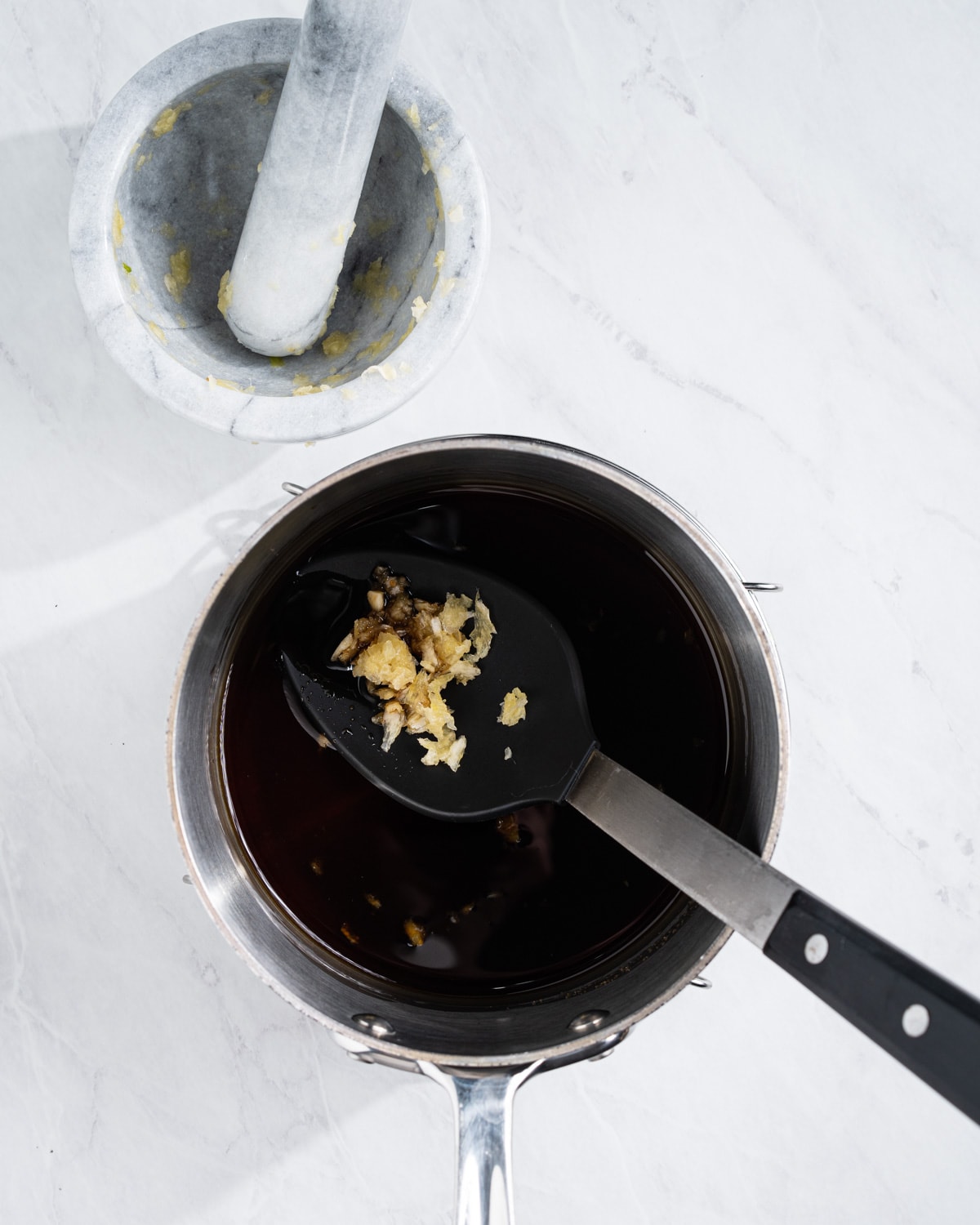 All of the eel sauce ingredients in a pot. Mortar and pestle with mashed garlic on the side.