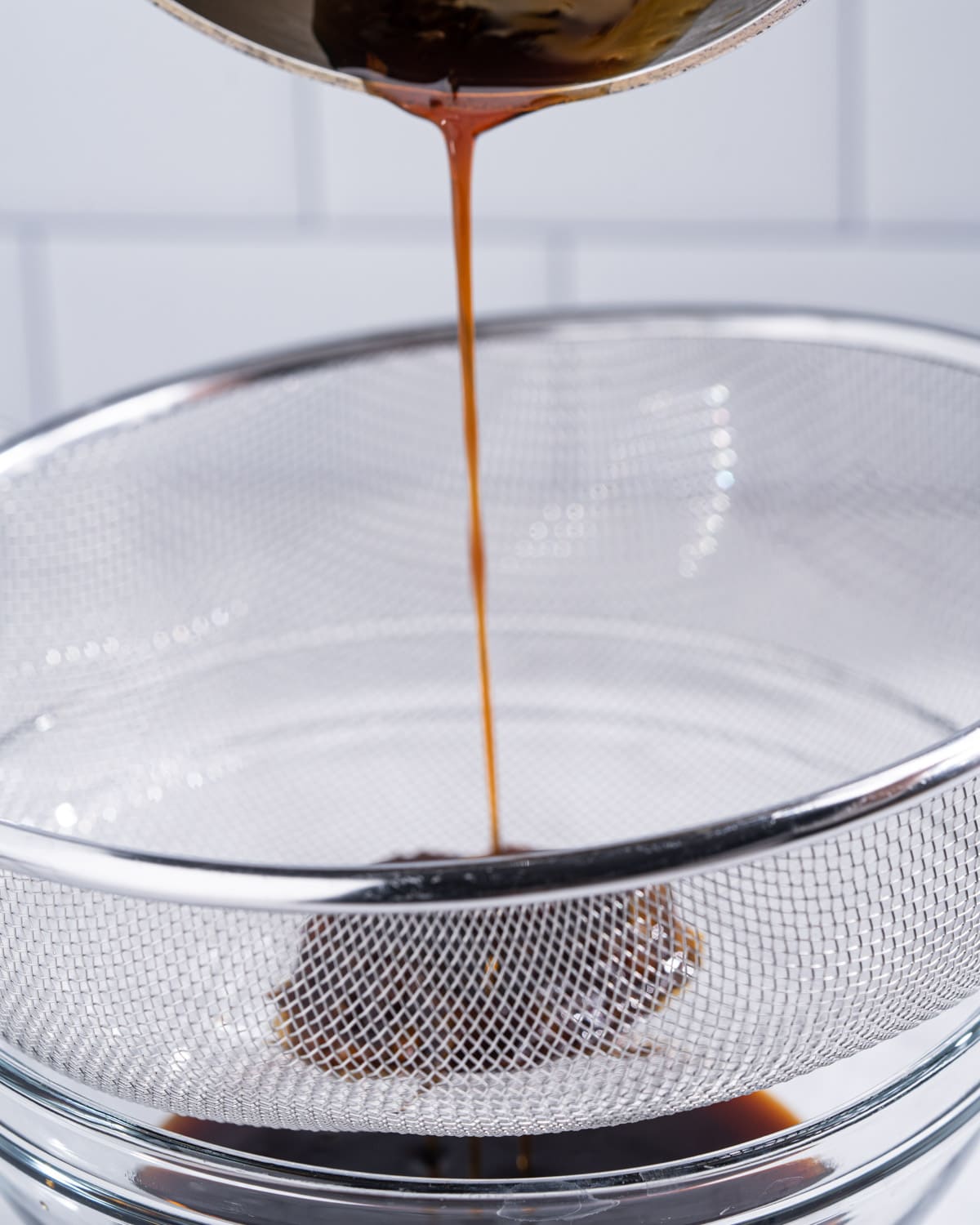 Pot of unagi eel sauce being poured through a fine mesh strainer.