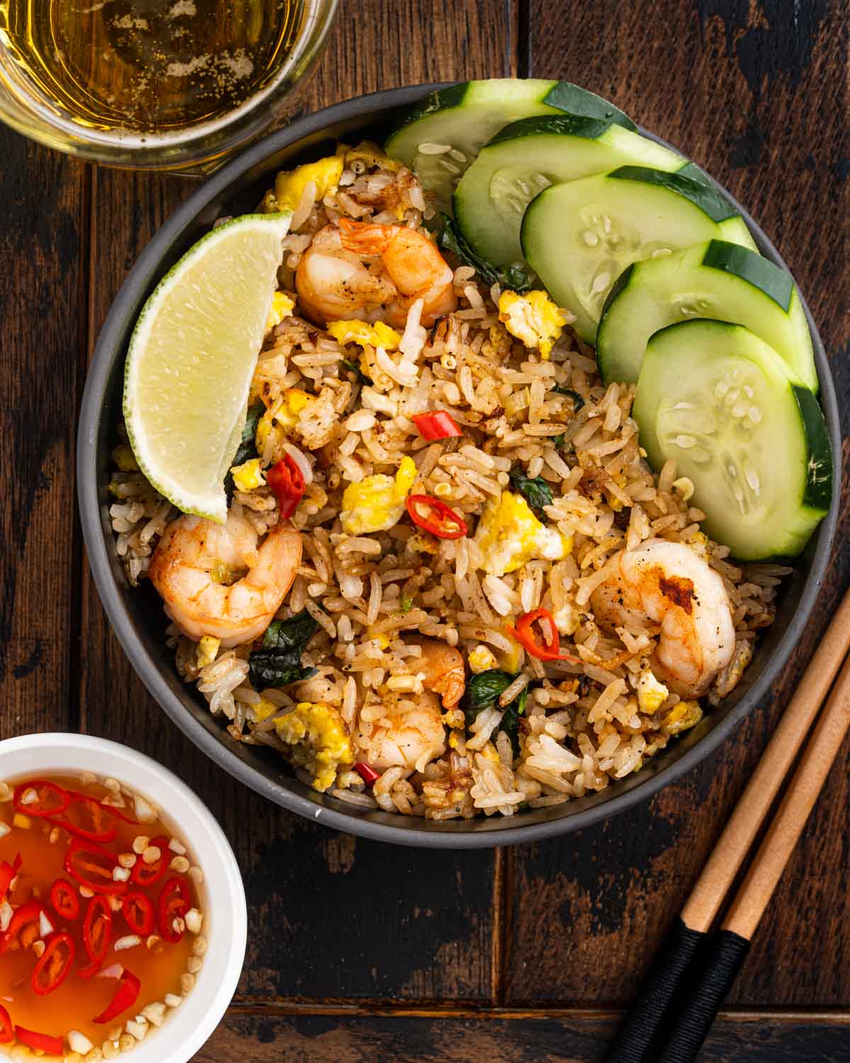 bowl of Thai fried rice with shrimp, garnished with lime wedge, and sliced cucumbers.