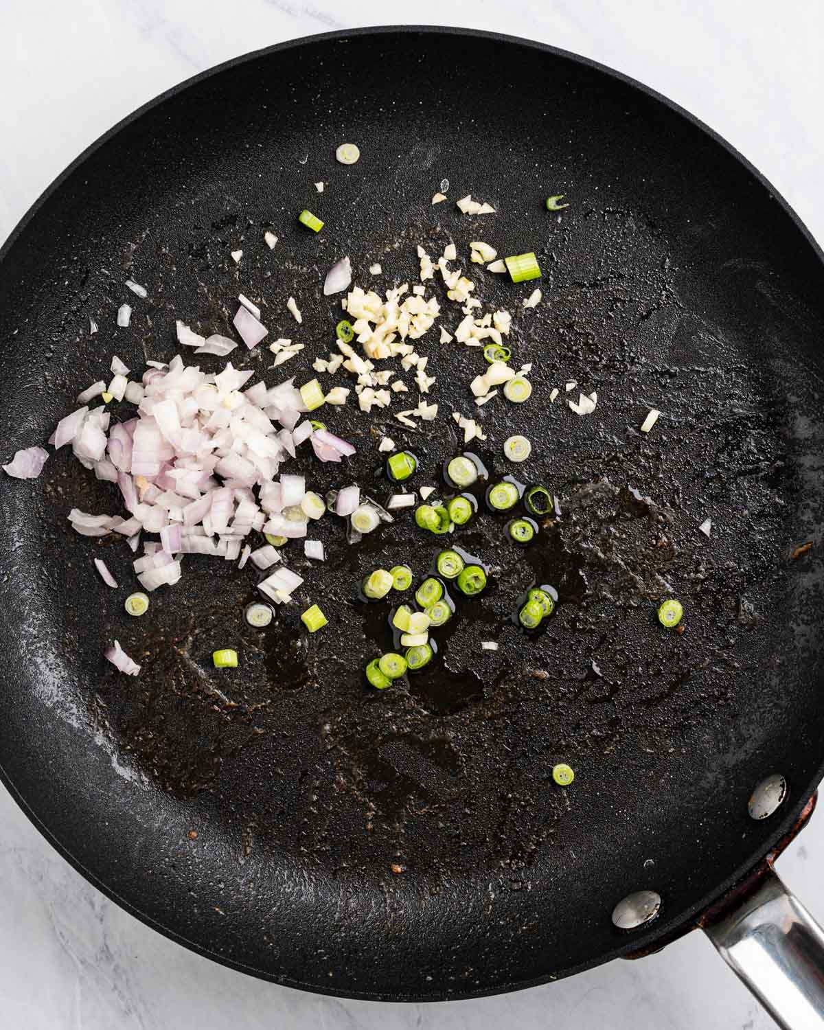 Pan with oil, diced shallots, chopped green onions, and minced garlic.