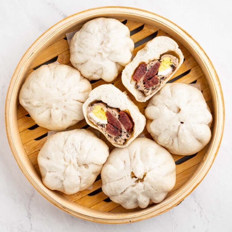 Banh bao steamed buns in a bamboo steamer basket. One cut in half to show inside.