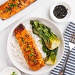 Table setup of Miso glazed salmon on plates of rice and baby bok choy.