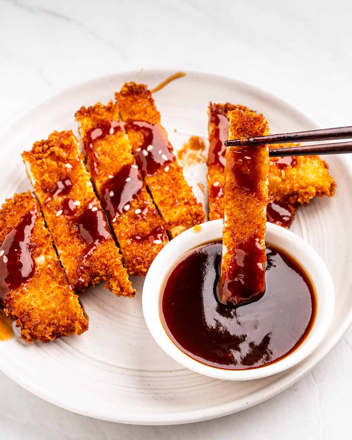 dipping piece of chicken katsu into katsu sauce.