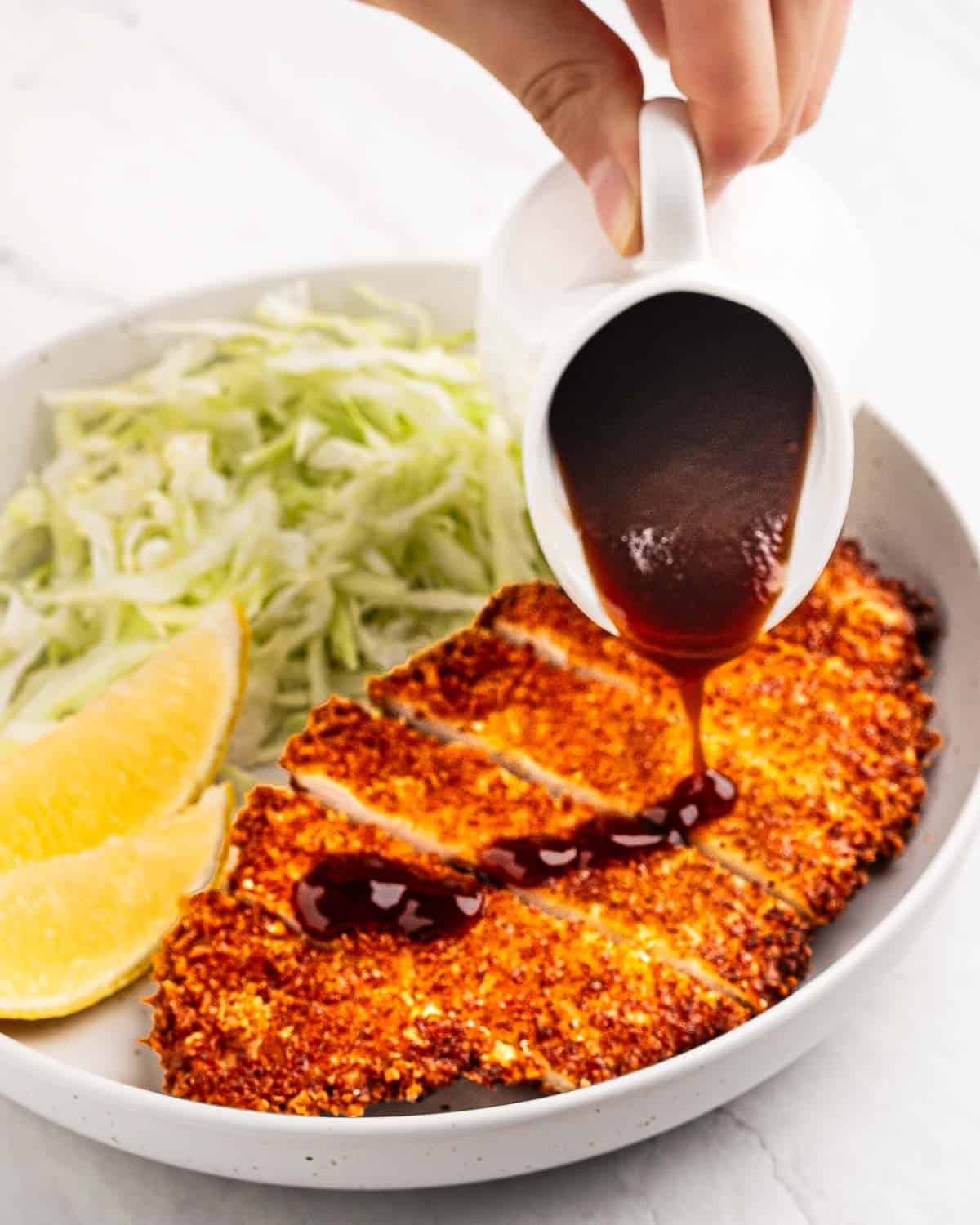 pouring tonkatsu sauce onto fried breaded chicken.