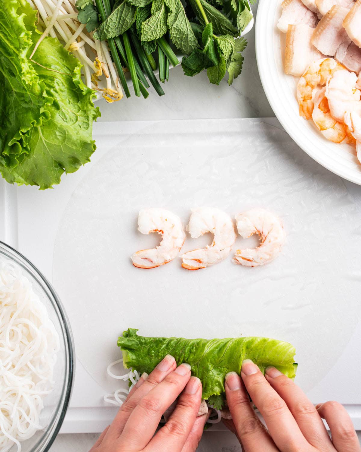 hands tucking in lettuce and herbs, shrimp placed at top of rice paper.