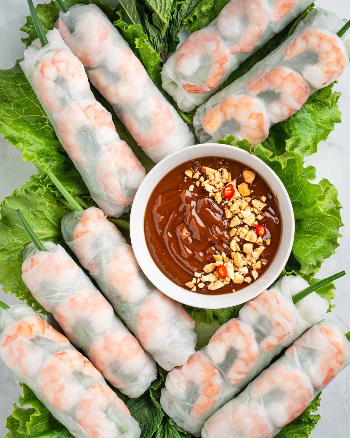 spring rolls on a bed of lettuce and herbs with dipping sauce.